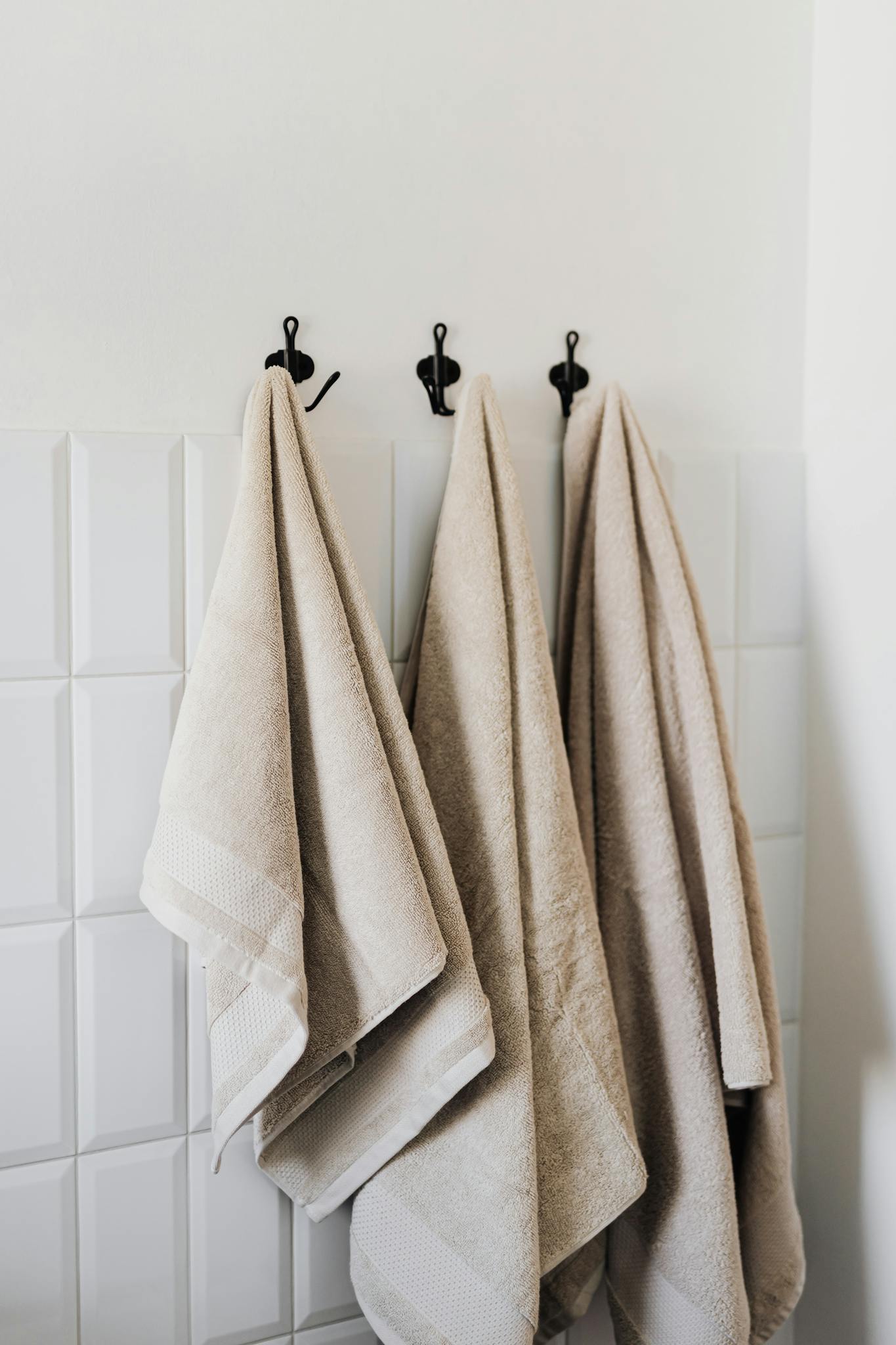 Beige hand towel and face towel and floor towel hooked in bathroom against white tiles in hotel room