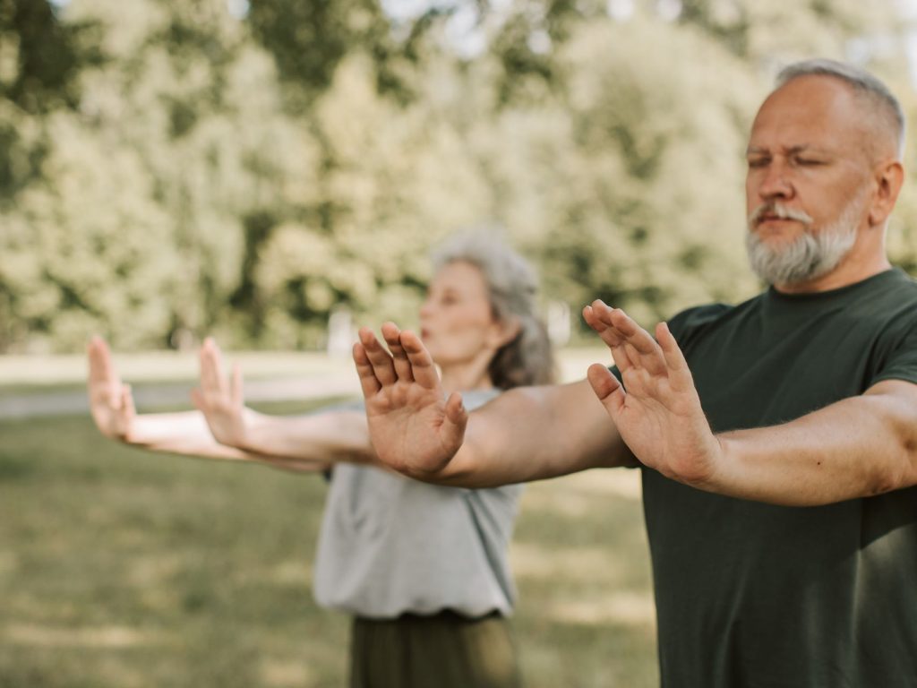 Elderly couple meditating and enjoying wellness outdoors with arms outstretched.